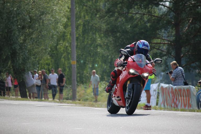 Muž v červenej kombinéze, na červenej motorke s prilbou na hlave ide po ceste